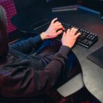 A person in a hoodie typing on a keyboard Description automatically generated