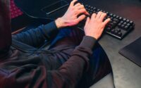 A person in a hoodie typing on a keyboard Description automatically generated